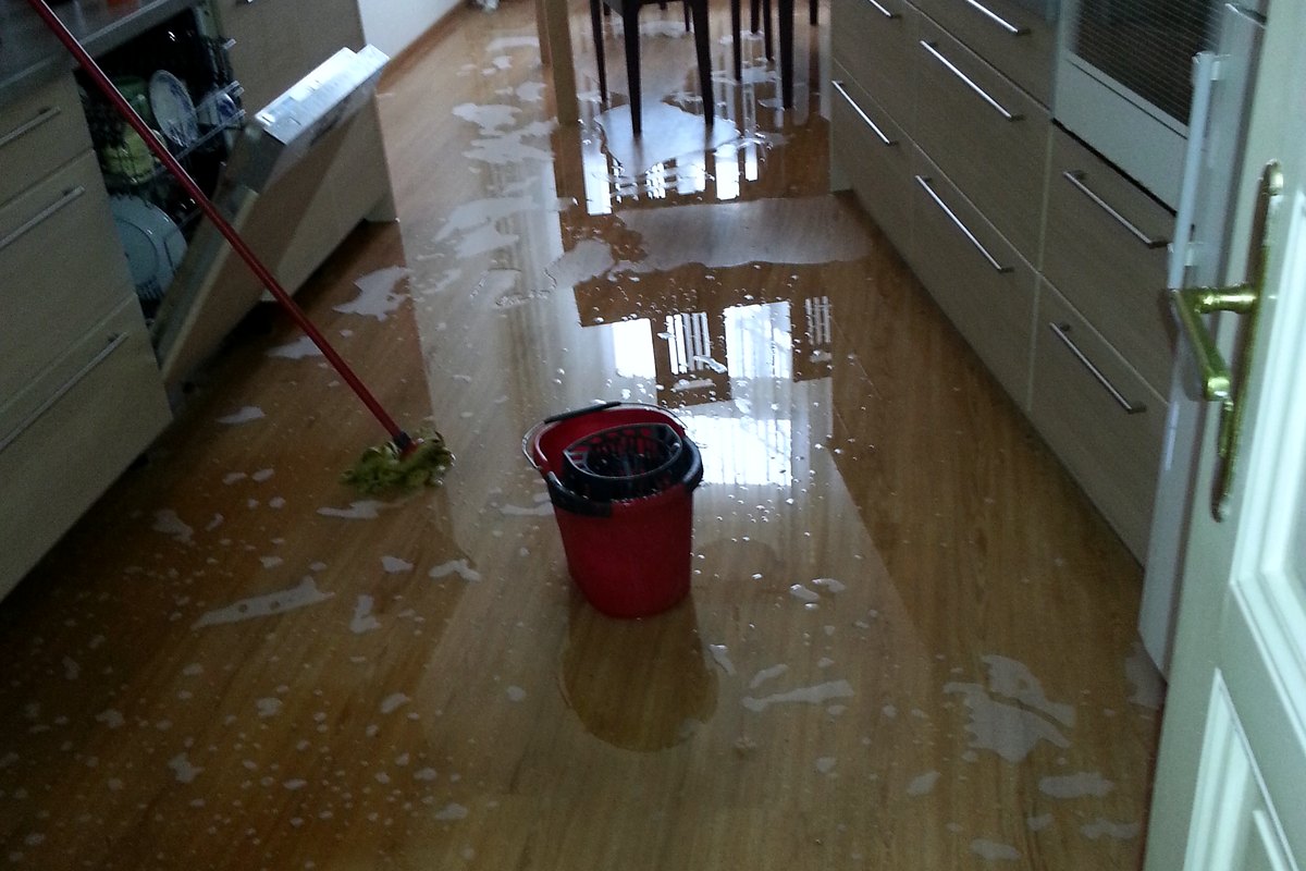 Cocina de una vivienda con el suelo encharcado, un cubo y una fregona en medio del agua